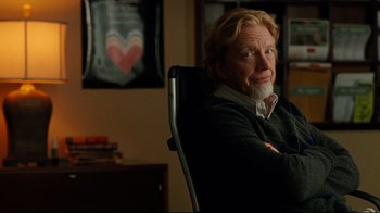 Movie still from “The Blind Side” (2009), directed by John Lee Hancock – A man sitting in a chair with his arms crossed; Medium shot, Over the shoulder angle