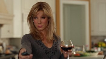 Movie still from “The Blind Side” (2009), directed by John Lee Hancock – A woman holding a glass of red wine while holding a remote control; Close Up shot, Over the shoulder angle