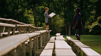 Movie still from “The Blind Side” (2009), directed by John Lee Hancock – A young boy standing on top of a wooden bench; Wide shot, Over the shoulder angle