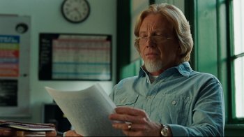 Movie still from “The Blind Side” (2009), directed by John Lee Hancock – An older man reading a paper in front of a wall clock; Close Up shot, Over the shoulder angle