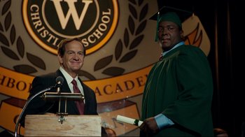 Movie still from “The Blind Side” (2009), directed by John Lee Hancock – Two men standing next to each other at a podium; Medium shot, Low angle