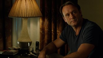 Movie still from “The Blind Side” (2009), directed by John Lee Hancock – A man sitting on a couch in a room; Close Up shot, Over the shoulder angle