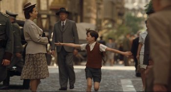 Movie still from “The Boy in the Striped Pajamas” (2008), directed by Mark Herman – A young boy is walking on the street with an older man and woman; Wide shot, Over the shoulder angle