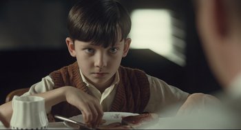 Movie still from “The Boy in the Striped Pajamas” (2008), directed by Mark Herman – A young boy sitting at a table with a plate of food in front of him; Close Up shot, Over the shoulder angle