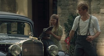 Movie still from “The Boy in the Striped Pajamas” (2008), directed by Mark Herman – A woman reading a magazine next to an old car; Medium shot, Over the shoulder angle