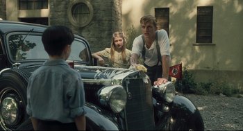 Movie still from “The Boy in the Striped Pajamas” (2008), directed by Mark Herman – A group of people standing next to an antique car; Medium shot, Over the shoulder angle