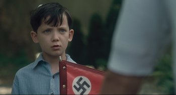 Movie still from “The Boy in the Striped Pajamas” (2008), directed by Mark Herman – A young boy is holding a nazi flag in front of a man; Close Up shot, Over the shoulder angle