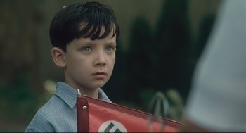 Movie still from “The Boy in the Striped Pajamas” (2008), directed by Mark Herman – A young boy holding a nazi flag while standing outside; Close Up shot, Over the shoulder angle