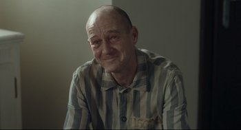 Movie still from “The Boy in the Striped Pajamas” (2008), directed by Mark Herman – An older man in a striped shirt sitting in a room; Close Up shot, Over the shoulder angle