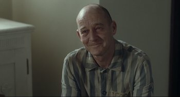 Movie still from “The Boy in the Striped Pajamas” (2008), directed by Mark Herman – A man with a shaved head is smiling for the camera; Close Up shot, Over the shoulder angle