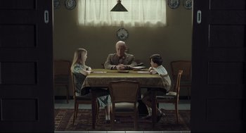 Movie still from “The Boy in the Striped Pajamas” (2008), directed by Mark Herman – A man sitting at a table with two young children; Wide shot, Over the shoulder angle