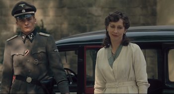 Movie still from “The Boy in the Striped Pajamas” (2008), directed by Mark Herman – A woman standing next to a car in front of a brick wall; Medium shot, Over the shoulder angle