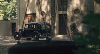 Movie still from “The Boy in the Striped Pajamas” (2008), directed by Mark Herman – An old car is parked in front of a building; Wide shot, High angle