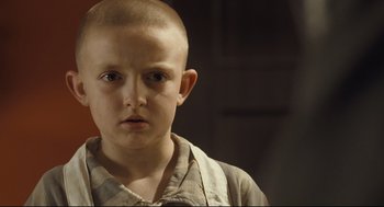 A boy with a shaved head is looking at the camera