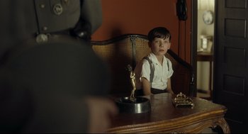 Movie still from “The Boy in the Striped Pajamas” (2008), directed by Mark Herman – A boy sitting in front of a table with a trophy; Medium shot, Over the shoulder angle