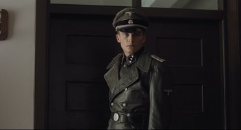 Movie still from “The Boy in the Striped Pajamas” (2008), directed by Mark Herman – A man in a leather jacket wearing a hat; Medium shot, Low angle