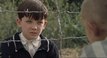 Movie still from “The Boy in the Striped Pajamas” (2008), directed by Mark Herman – A young boy standing behind a barbed wire fence; Close Up shot, High angle