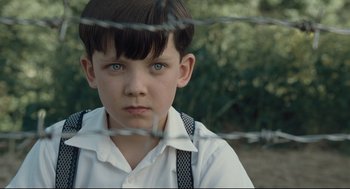 Movie still from “The Boy in the Striped Pajamas” (2008), directed by Mark Herman – A young boy with blue eyes is behind barbed wire; Close Up shot, High angle