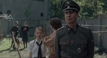 Movie still from “The Boy in the Striped Pajamas” (2008), directed by Mark Herman – A man in a military uniform stands next to a girl; Medium shot, Over the shoulder angle