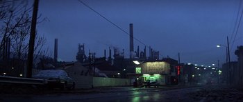 Movie still from “The Deer Hunter” (1978), directed by Michael Cimino – A car driving down a street near a factory; Extreme Wide shot, High angle