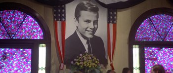 Movie still from “The Deer Hunter” (1978), directed by Michael Cimino – A portrait of a young man in front of american flags; Medium shot, Low angle