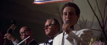 Movie still from “The Deer Hunter” (1978), directed by Michael Cimino – A man in a white suit is holding a microphone and another man in a white suit is holding a microphone; Close Up shot, Low angle