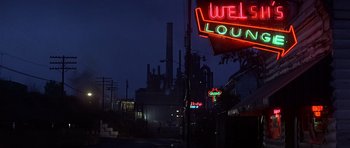 Movie still from “The Deer Hunter” (1978), directed by Michael Cimino – A neon sign that reads " welcome " in front of an industrial area at night; Extreme Wide shot, Low angle