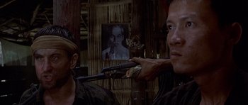 Movie still from “The Deer Hunter” (1978), directed by Michael Cimino – A man holding a rifle in front of a picture of a man; Close Up shot, Over the shoulder angle