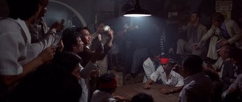 Movie still from “The Deer Hunter” (1978), directed by Michael Cimino – A group of people sitting around a room with a light on; Wide shot, High angle