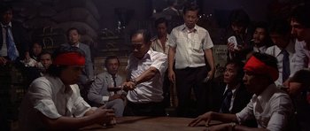 Movie still from “The Deer Hunter” (1978), directed by Michael Cimino – A group of men standing around a wooden table; Medium shot, Over the shoulder angle