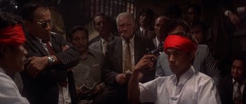 Movie still from “The Deer Hunter” (1978), directed by Michael Cimino – A group of people in a room with a man smoking a cigarette; Medium shot, High angle