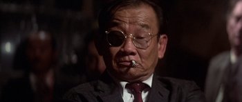 Movie still from “The Deer Hunter” (1978), directed by Michael Cimino – An older man wearing glasses and a suit smoking a cigarette; Close Up shot, Low angle