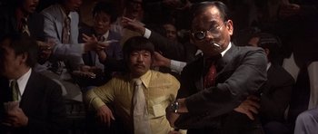 Movie still from “The Deer Hunter” (1978), directed by Michael Cimino – A group of men in suits and ties in front of a crowd; Medium shot, Low angle