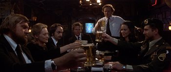 Movie still from “The Deer Hunter” (1978), directed by Michael Cimino – A group of people sitting at a table with drinks; Medium shot, Low angle