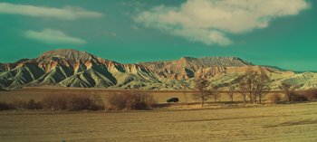 Movie still from “10 Days of a Bad Man” (2023), directed by Uluç Bayraktar – A car is parked in the middle of a field; Extreme Wide shot, High angle