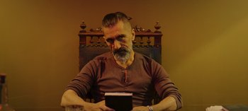 Movie still from “10 Days of a Bad Man” (2023), directed by Uluç Bayraktar – A man sitting in front of a box on top of a table; Medium shot, Low angle