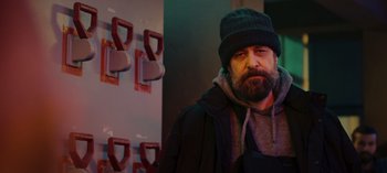 Movie still from “10 Days of a Bad Man” (2023), directed by Uluç Bayraktar – A man with a beard wearing a hat and a jacket; Medium shot, Low angle