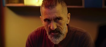 Movie still from “10 Days of a Bad Man” (2023), directed by Uluç Bayraktar – An older man with a beard and a mustache; Close Up shot, Over the shoulder angle