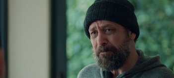 Movie still from “10 Days of a Bad Man” (2023), directed by Uluç Bayraktar – A person with a beard wearing a hat; Close Up shot, Over the shoulder angle