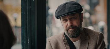 Movie still from “10 Days of a Bad Man” (2023), directed by Uluç Bayraktar – A man with a beard wearing a hat and a jacket; Close Up shot, Over the shoulder angle