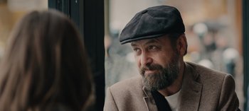 Movie still from “10 Days of a Bad Man” (2023), directed by Uluç Bayraktar – A man with a beard wearing a hat and a suit; Close Up shot, Over the shoulder angle