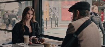 Movie still from “10 Days of a Bad Man” (2023), directed by Uluç Bayraktar – A woman sitting at a table in front of a window; Medium shot, Over the shoulder angle