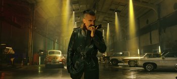 Movie still from “10 Days of a Bad Man” (2023), directed by Uluç Bayraktar – A man in a black leather jacket is smoking a cigarette in a parking lot; Medium shot, Low angle