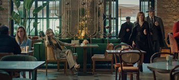 Movie still from “10 Days of a Bad Man” (2023), directed by Uluç Bayraktar – A woman sitting at a table in front of a green couch; Wide shot, Low angle