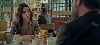 Movie still from “10 Days of a Bad Man” (2023), directed by Uluç Bayraktar – A woman sitting at a table with a cup of coffee; Medium shot, Over the shoulder angle