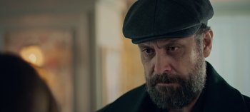 Movie still from “10 Days of a Bad Man” (2023), directed by Uluç Bayraktar – A man with a beard wearing a hat and jacket; Close Up shot, Over the shoulder angle