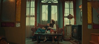 Movie still from “10 Days of a Bad Man” (2023), directed by Uluç Bayraktar – A man and a woman sitting on a couch in a living room; Wide shot, Low angle