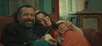 Movie still from “10 Days of a Bad Man” (2023), directed by Uluç Bayraktar – A man and a woman smile while holding a piece of food; Medium shot, High angle