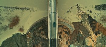 Movie still from “10 Days of a Bad Man” (2023), directed by Uluç Bayraktar – An aerial view of a car driving on a road; Extreme Wide shot, Overhead angle
