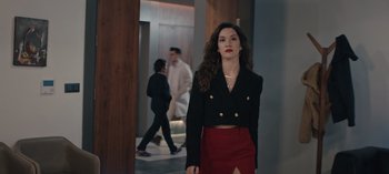 Movie still from “10 Days of a Bad Man” (2023), directed by Uluç Bayraktar – A woman in a black jacket and red skirt standing in a hallway; Medium shot, Low angle